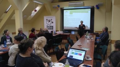 Zdjęcie przedstawia grupę osób słuchających kobiety szkoleniowaca.