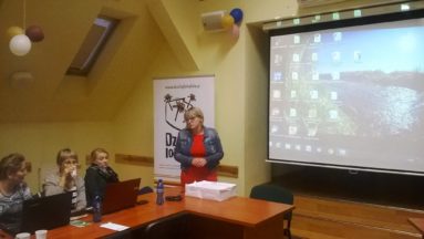 Zdjęcie przedstawia osoby słuchające szkoleniowca kobietę. W tle ekran projektora.