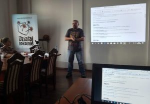 21 Zdjęcie przedstawia mężczyznę przemawiającego do grupy osób, którzy siedzą przy stołach
