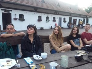 Zdjęcie przedstawia pięć os&oacute;b siedzących przy&nbsp;stole i&nbsp;słuchających osoby przemawiającej