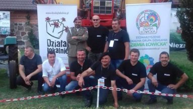 Członkowie Stowarzyszenia Miłośników  Starej Motoryzacji i Maszyn Rolniczych Retro-Łowiczanka w plenerze, w tle rollup z logo Działaj Lokalnie oraz Stowarzyszenia LGD ,,Ziemia Łowicka”