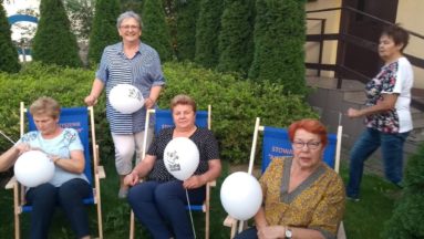 Panie ze Stowarzyszenia ,,Aktywny Senior” relaksujące się na leżakach wśród zieleni, w ręku trzymają balony z logo Działaj Lokalnie.