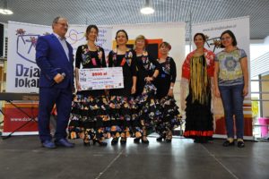 Zdjęcie przedstawia grupę os&oacute;b pozujących do&nbsp;zdjęcia. Cztery kobiety ubrane w&nbsp;suknie do&nbsp;flamenco trzymają symboliczny czek na&nbsp;grant programu Działaj Lokalnie.