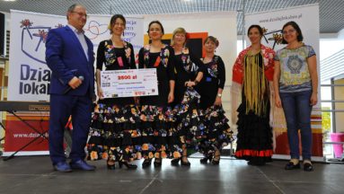 Zdjęcie przedstawia grupę osób pozujących do zdjęcia. Cztery kobiety ubrane w suknie do flamenco trzymają symboliczny czek na grant programu Działaj Lokalnie.