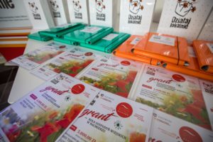 Zdjęcie przedstawia ułożone na&nbsp;stole materiały promocyjne "Działaj Lokalnie" oraz&nbsp;symboliczne czeki dla&nbsp;zwycięzc&oacute;w konkursu.