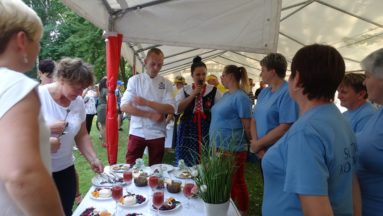 Zdjęcie przedstawia grupę ludzi stojącą przy stole zastawionym potrawami.