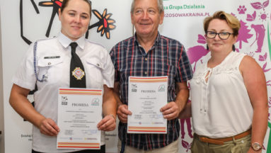Zdjęcie przedstawia trzy osoby z uśmiechem pozujące do zdjęcia. Dwie z nich trzymają podpisane promesy na granty.