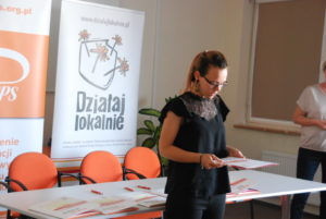 Laureaci konkursu Działaj Lokalnie 2019 Zdjęcie przedstawia przemawiającą osobę, stojącą na tle banerów POPPS i programów Działaj Lokalnie.