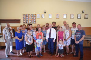 Mieszkańcy wsi Korzeń Zdjęcie przedstawia wilopokoleniową grupę mieszkańców wsi, pozujących do zdjęcia we wnętrzu.