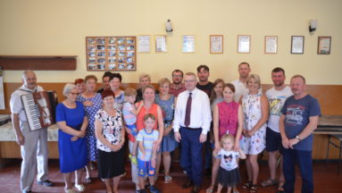 Zdjęcie przedstawia wilopokoleniową grupę mieszkańców wsi, pozujących do zdjęcia we wnętrzu.