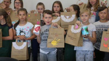 Zdjęcie przedstawia grupę dzieci pozujących do zdjęcia z własnoręcznie wykonanymi papierowymi torbami.