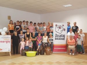 Zdjęcie przedstawia grupę os&oacute;b pozujących do&nbsp;zdjęcia we wnętrzu, dookoła baneru z&nbsp;logiem programu Działaj Lokalnie.