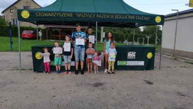 Zdjęcie przedstawia dzieci pozujące do zdjęcia przed namiotem z napisem "Stowarzyszenie Wszyscy Razem w Bogucinie Dużym".