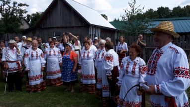 Zdjęcie przedstawia grupę osób ubraną w tradycyjne ludowe stroje, stojącą na zewnątrz.
