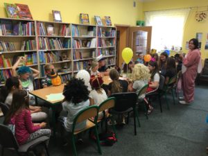 Warsztaty biblioteczne Zdjęcie przedstawia dzieci poprzebierane w różne stroje, siedzące przy stolikach w bibliotece.