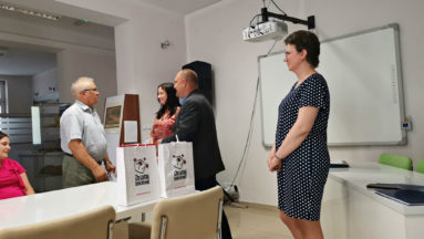 Na zdjęciu widzimy cztery osoby stojące przy stole, na którym znajdują się torby z logiem programu "Działaj Lokalnie".