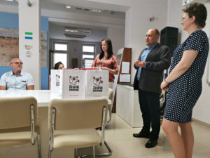 Zdjęcie przedstawia pięć os&oacute;b stojących przy&nbsp;stole we wnętrzu. Na&nbsp;stole stoją torby z&nbsp;logiem programu "Działaj Lokanie".