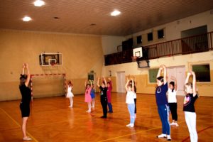 Zdjęcie przedstawia uczestnik&oacute;w zajęć baletu dla&nbsp;dzieci na&nbsp;sali gimnastycznej podczas ćwiczeń.