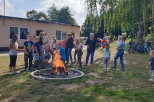 Zdjęcie przedstawia grupę os&oacute;b stojących przy&nbsp;ognisku.