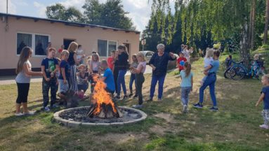 Zdjęcie przedstawia grupę osób stojących przy ognisku.
