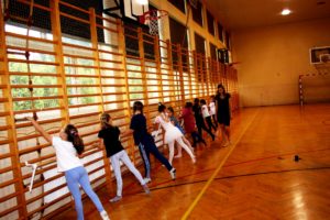 Zdjęcie przedstawia uczestnik&oacute;w zajęć baletu dla&nbsp;dzieci na&nbsp;sali gimnastycznej podczas rozgrzewki.