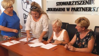 Zdjęcie przedstawia osoby przy stole we wnętrzu, podpisujące umowy.