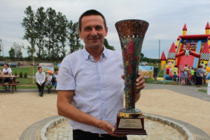 Zdjęcie przedstawia mężczyznę w&nbsp;białej koszuli, prezentującego puchar.