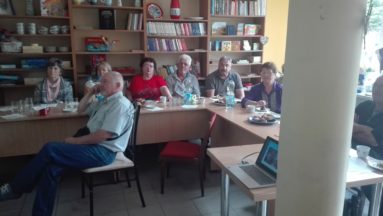Zdjęcie przedstawia osoby słuchające wykładu w bibliotece.