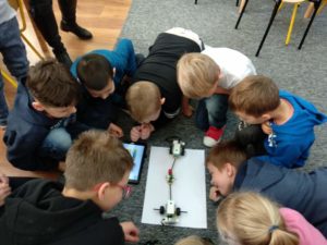 Mobilna robotyka pod lupą Zdjęcie przedstawia grupkę dzieci, pochyloną nad robotem z klocków Lego stojącym na podłodze.