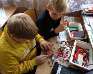 Zdjęcie przedstawia dw&oacute;jkę dzieci przy&nbsp;stole, układających robota z&nbsp;klock&oacute;w Lego.