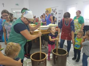 Na zdjęciu dzieci i&nbsp;młodzież, pod&nbsp;czujnym okiem babć, ubijają kapustę w&nbsp;garnku.