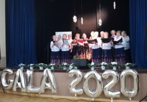 Występ zespołów wokalnych "Jarzębina" i "Prośliczanki" Zdjęcie przedstawia osoby z zespołu, ubrane w tradycyjne stroje, występujące podczas gali.