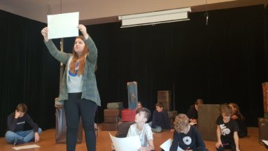 Zdjęcie przedstawia grupę młodzieży na scenie podczas próby do spektaklu.