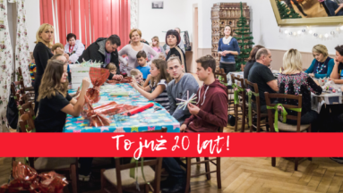 Zdjęcie przedstawia osoby siedzące przy stolikach podczas spotkania wigilijnego organizowanego w ramach "Działaj Lokalnie". Na zdjęcie nałożony jest napis "To już 20 lat!".