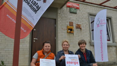 Zdjęcie przedstawia osoby pozujące do zdjęcia przed budynkiem, pokazujące podpisane umowy.