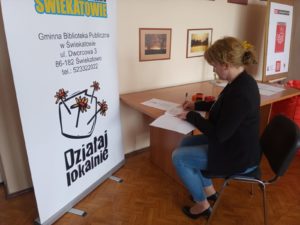 Zdjęcie przedstawia osobę przy&nbsp;biurku, obok&nbsp;banera Działaj Lokalnie, podpisującą umowę.