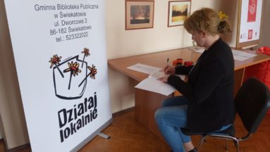 Zdjęcie przedstawia osobę przy biurku, obok banera Działaj Lokalnie, podpisującą umowę.