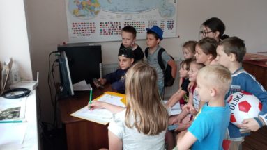 Zdjęcie przedstawia grupę dzieci przed komputerem.