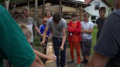 Uczestnicy projektu sprawdzają swoje siły w heblowaniu drzewa, które będzie wykorzystane do budowy pojazdu Flinstonów.