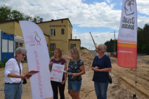 Stąd jesteśmy Zdjęcie przedstawia grupę osób stojącą na zewnątrz, obok banerów z logiem Działaj Lokalnie i Fundacji Koalicji dla Młodych.