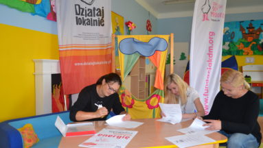 Zdjęcie przedstawia osobę podpisującą umowę pod banerem "Działaj Lokalnie"
