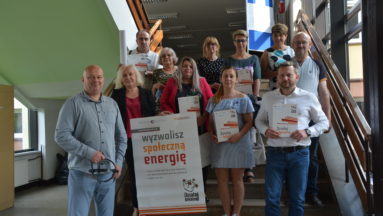 Zdjęcie przedstawia grupę osób w pomieszczeniu, pozujących do zdjęcia, trzymających plakat z napisem "Wyzwolisz społeczną energię"