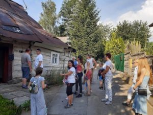 Uczestnicy oglądający starą drewnianą chatę.