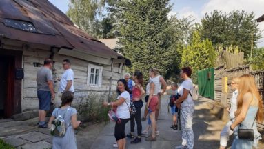 Uczestnicy oglądający starą drewnianą chatę.