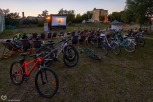 Zdjęcie przedstawia kino plenerowe - widownia siedzi na&nbsp;leżakach, a&nbsp;obok&nbsp;stoją ich rowery.