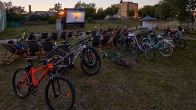 Zdjęcie przedstawia kino plenerowe - widownia siedzi na leżakach, a obok stoją ich rowery.