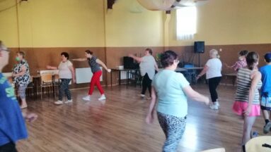 Grupa osób w sali maszeruje z kijkami do nordic walking