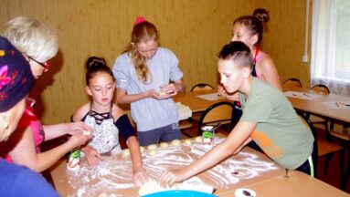 Grupa dzieci i seniorek formuje ciasto na pączki