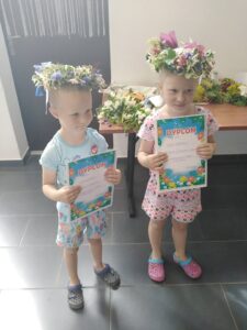 Noc świętojańska Dzieci z wiankami na głowie pozują do zdjęcia, pokazując swoje dyplomy