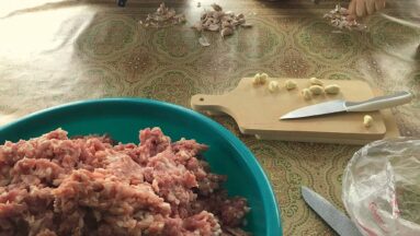 Na zdjęciu widać miskę z mięsem stojącą na stole i ręce osoby przygotowującej potrawę